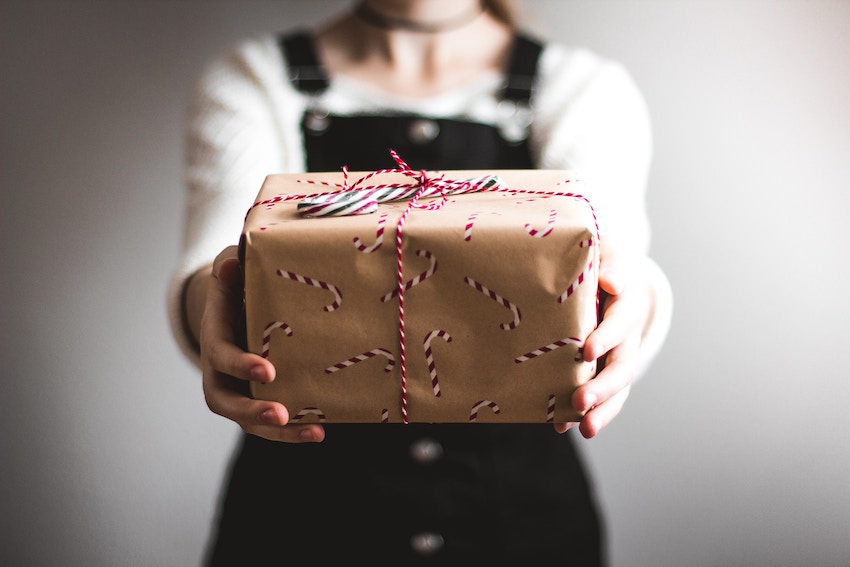 Chica sujeta paquete de regalo con bastones de caramelo en el envoltorio para representar el concepto actividades de Navidad en Alzamora